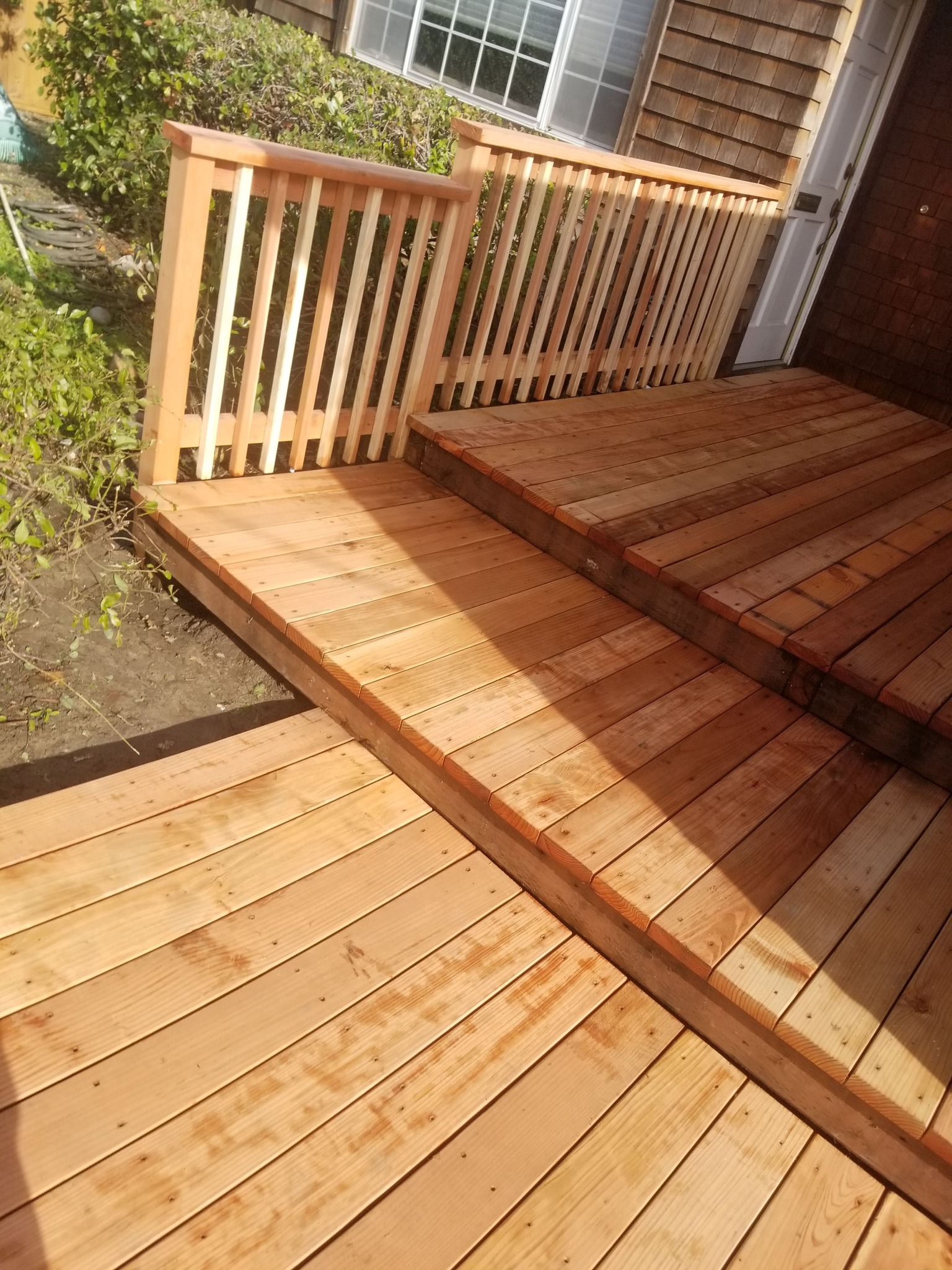 Freshly built exterior deck steps with new railings beside a front entry.